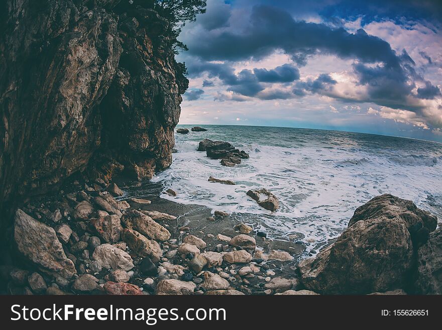 Rocky seashore. Strong waves and wind. Storm. Ocean against the background of the cloudy sky. Big stones on the seashore