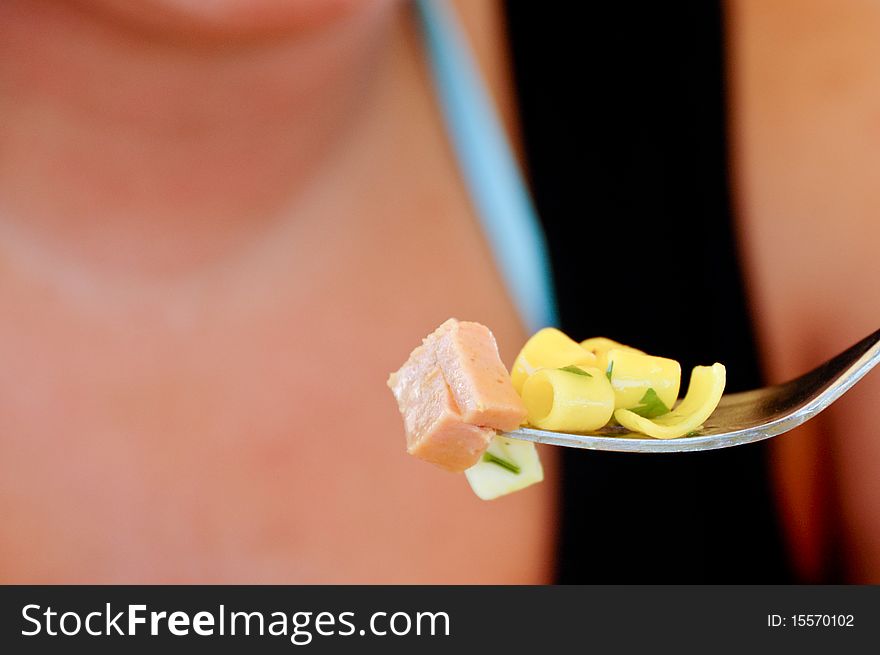 Girl eating cold meat and pasta with a fork. Background is the body of the girl.
Subject is the food so the girl is blurred.
Fork is positioned in a power point on right.