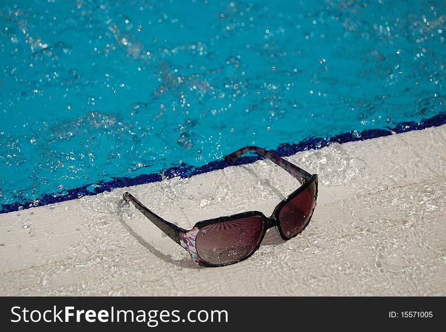 Splashed sunglasses lying by a swimming pool. Splashed sunglasses lying by a swimming pool