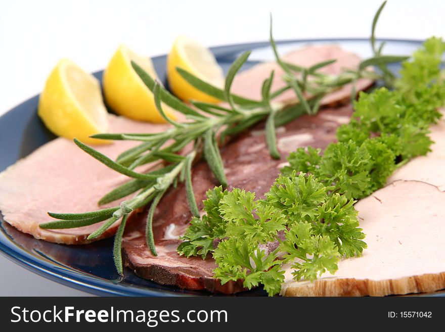 Plate of assorted cold cuts (ham, sirloin, headcheese) decorated with rosemary, parsley and lemon