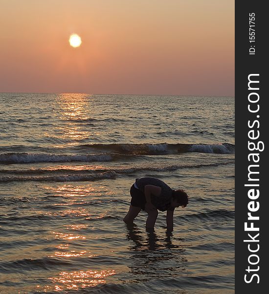 Teen girl looking for shells on beach at sunset. Teen girl looking for shells on beach at sunset