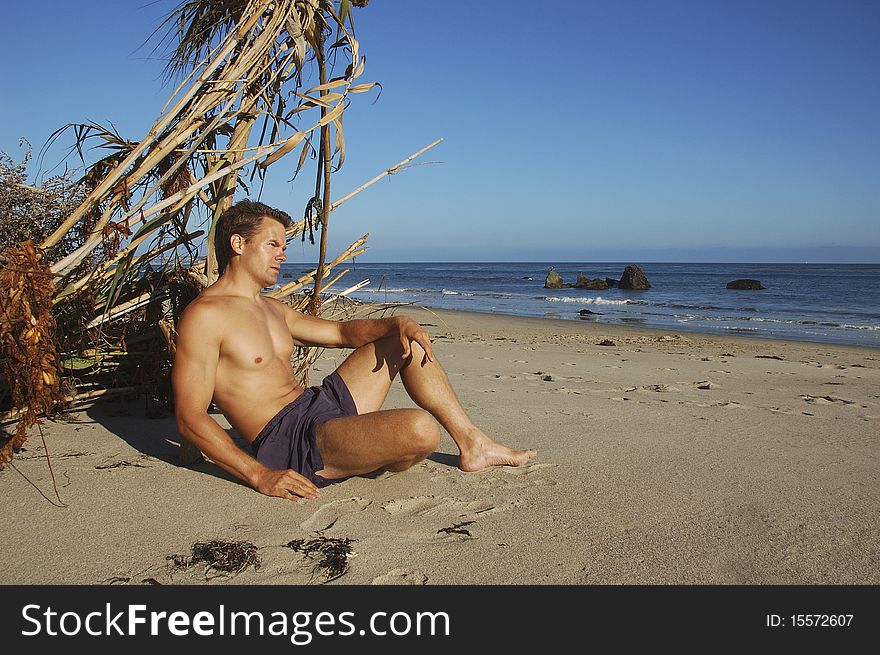 Vagabond man relaxing next to makeshift shelter on beautiful beach. Vagabond man relaxing next to makeshift shelter on beautiful beach