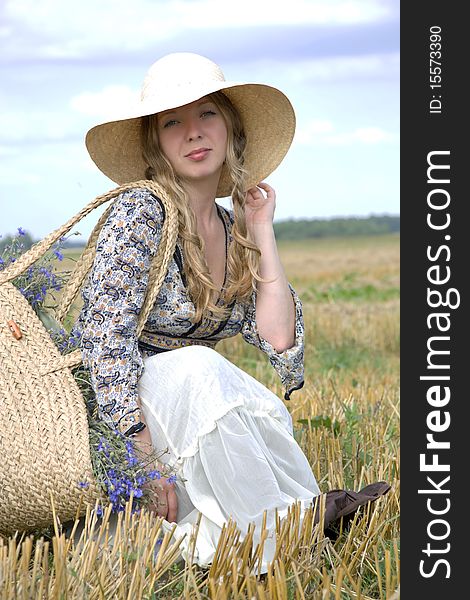 Woman in a hat sits in the summer in the field of with a basket of cornflowers. Woman in a hat sits in the summer in the field of with a basket of cornflowers