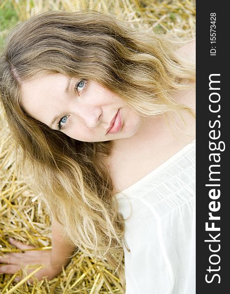 Woman with long hair and blue eyes sits and looks upwards in the summer on straw. Woman with long hair and blue eyes sits and looks upwards in the summer on straw
