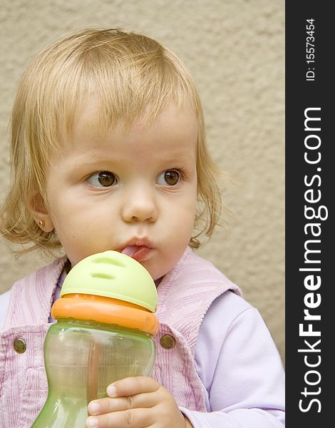 Little girl drinks from a small bottle and with interest looks aside. Little girl drinks from a small bottle and with interest looks aside