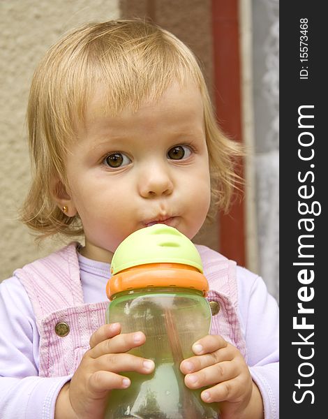 Little girl drinks from a small bottle and with interest looks aside. Little girl drinks from a small bottle and with interest looks aside