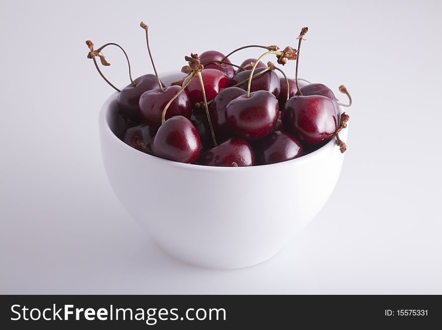 A white bowl of cherries on a white background.