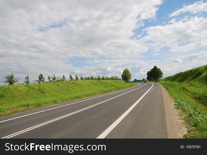 A deserted country road running through some green fields