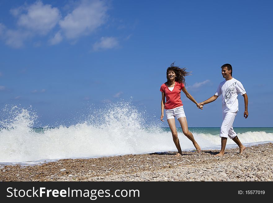 Young attractive couple holding hands while walking on the beach