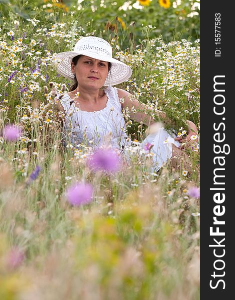 Lady in white dress and hat on a field with camomiles