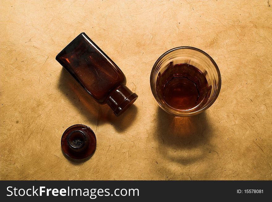 Medicin bottle and glas with brown liquide from above. Medicin bottle and glas with brown liquide from above.