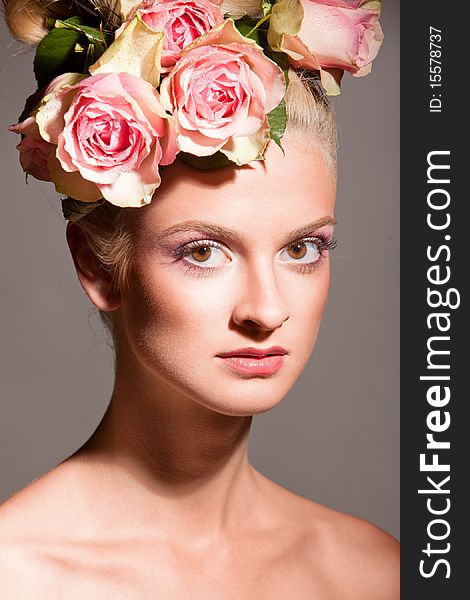 Portrait of beautiful blonde with a wreath of flowers on her head on the grey background