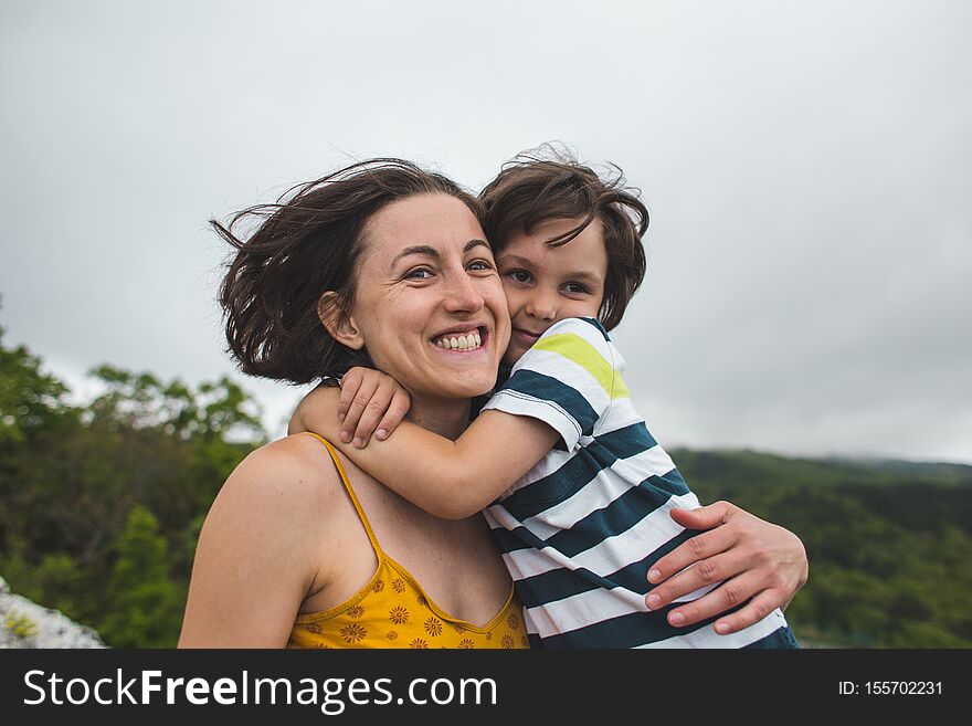 The boy hugs mom. Woman rests with her son in nature. The child kisses mom. Portrait of a mother and baby