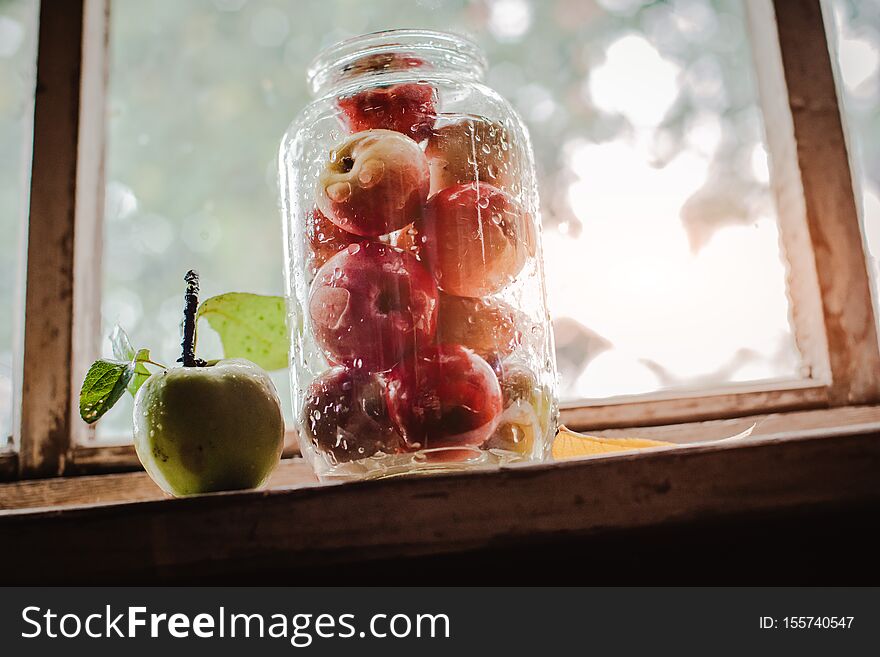 Fresh harvest of ripe and healthy farm apples in a glass jar, in a basket. Still life autumn rustic by the window and an old chest of drawers on a dark background