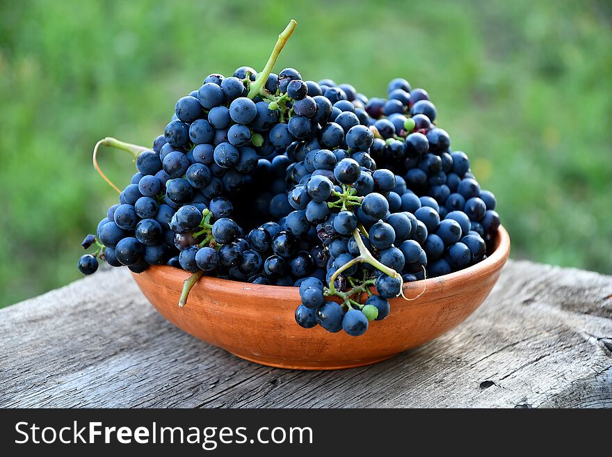 Black grapes in a ceramic plate on an old board in the garden.