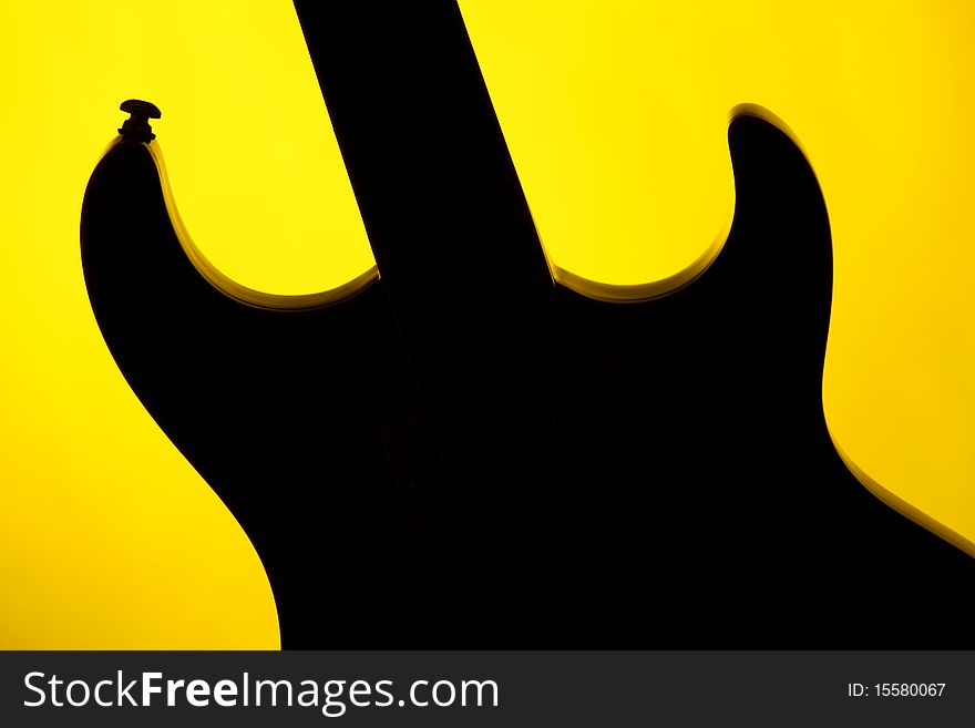 An electric guitar Silhouette isolated against a yellow background in the horizontal format. An electric guitar Silhouette isolated against a yellow background in the horizontal format.
