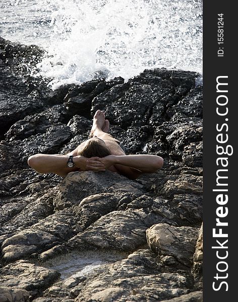 A color portrait photo of a caucasian man laying down on rocks and sunbathing next to the sea. A color portrait photo of a caucasian man laying down on rocks and sunbathing next to the sea.