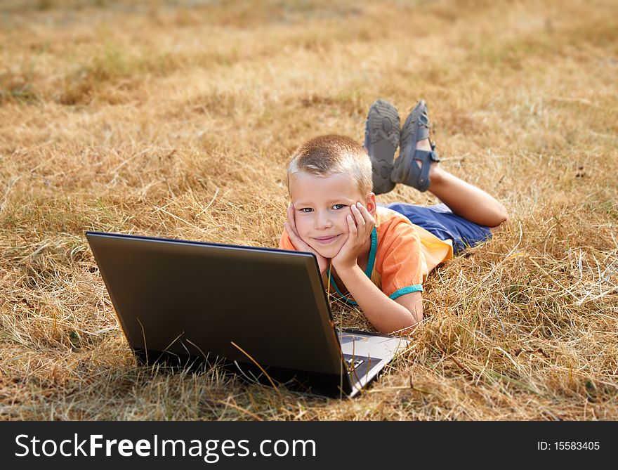 A smiling young boy laying on ground with laptop