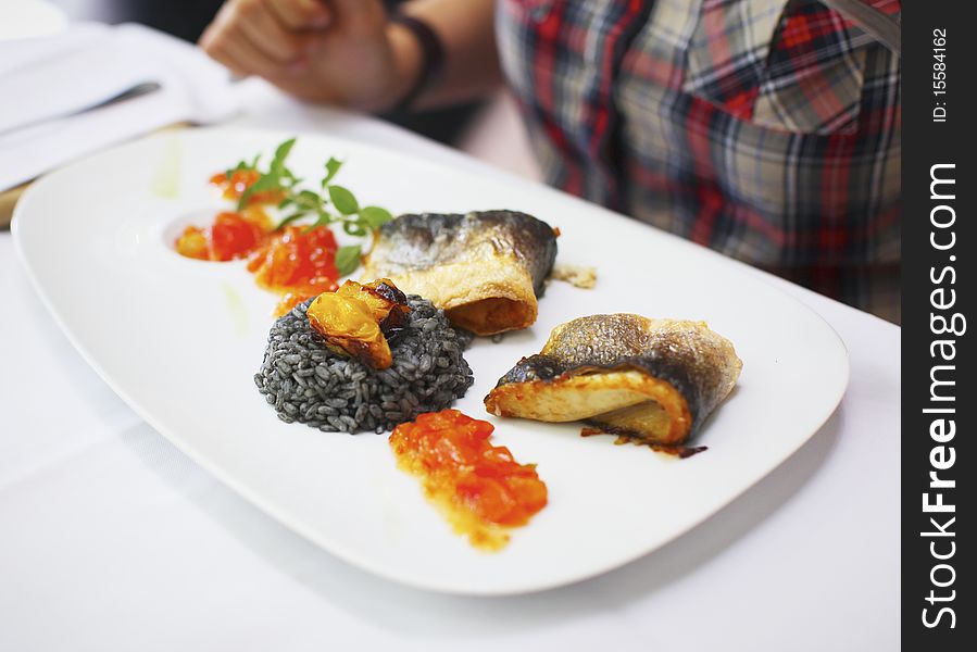 Fish fillet with black risotto and tomato relish on the sides.