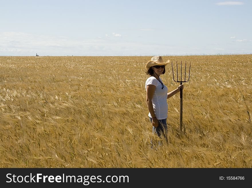Woman smiles holding a hay fork in a grain field. Woman smiles holding a hay fork in a grain field