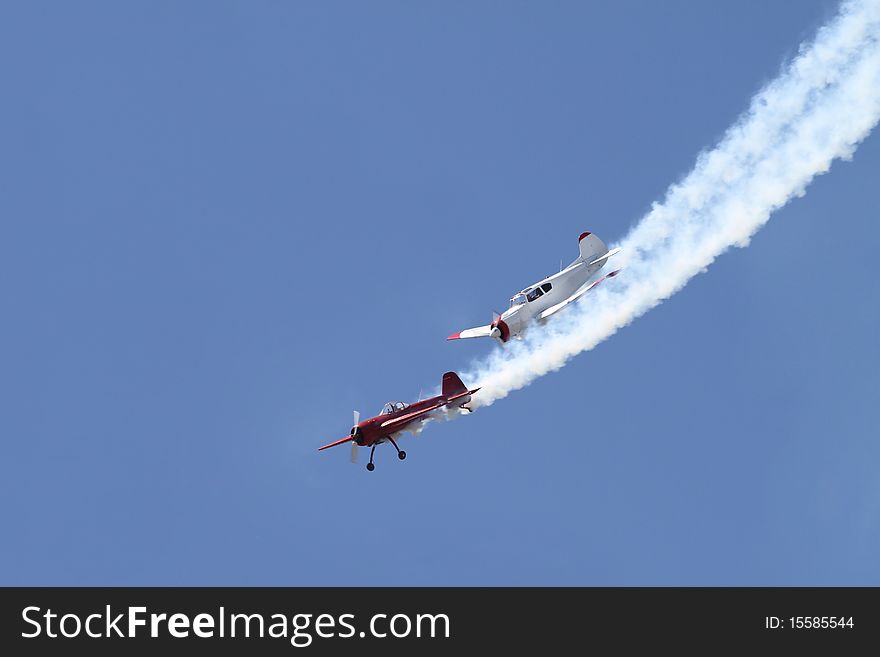 Two stunt planes fly in close formation at airshow. Smoke and blue sky in background. Two stunt planes fly in close formation at airshow. Smoke and blue sky in background.