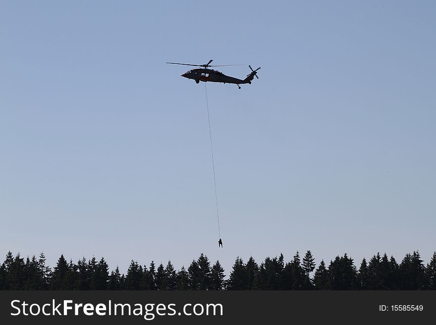 A helicopter hoists a person on a line from the forest. A helicopter hoists a person on a line from the forest.