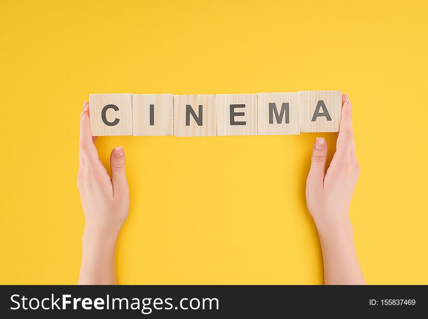 Top view of hands holding wooden cubes with cinema lettering isolated on yellow