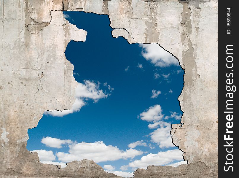 The hole in the cracked old wall, through which is visible the dark blue sky with clouds