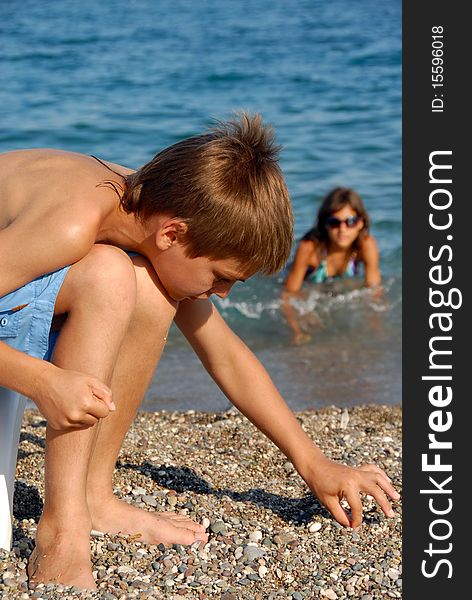 Little boy playing with rocks on pebble beach by blue sea. Little boy playing with rocks on pebble beach by blue sea