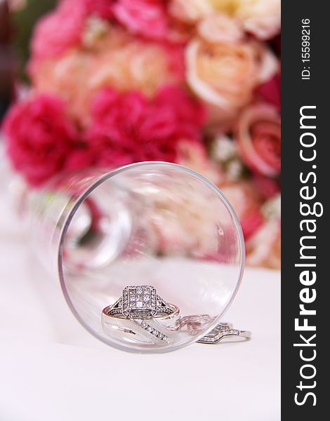 Wedding bands inside of a champagne glass. Colored roses in the background. Wedding bands inside of a champagne glass. Colored roses in the background.