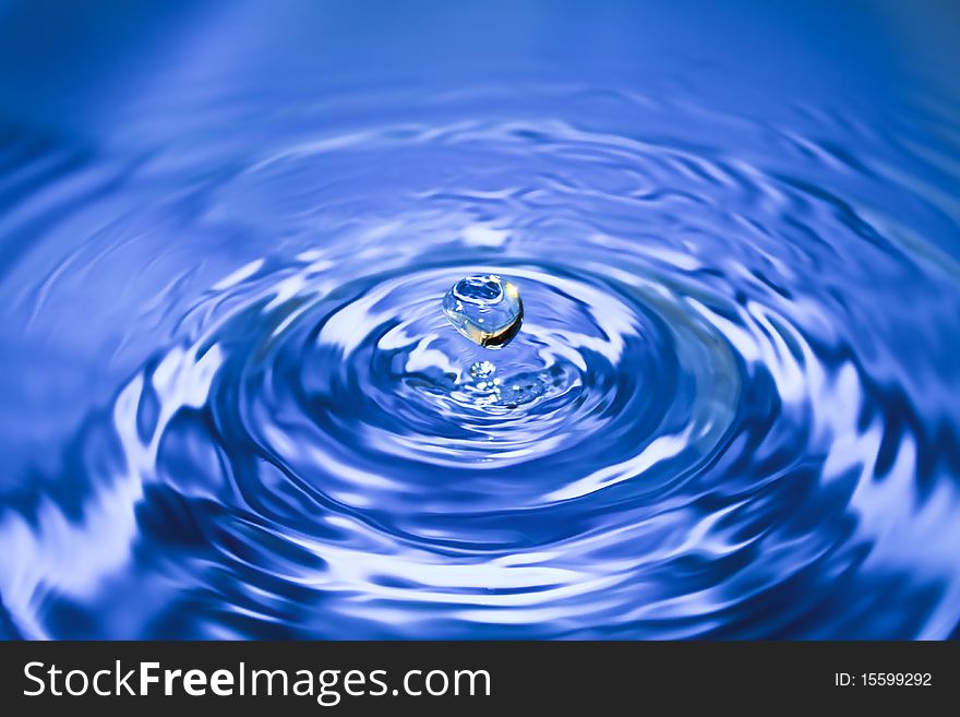 Clean blue drop of water splashing in clear water. Abstract blue background