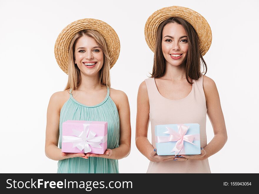 Two cheerful pretty young girls wearing summer outfit standing isolated over white background, showing present boxes. Two cheerful pretty young girls wearing summer outfit standing isolated over white background, showing present boxes