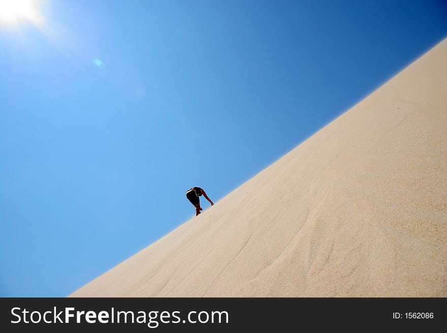 A man is climbing a sand dune in the mid day's sun. A man is climbing a sand dune in the mid day's sun