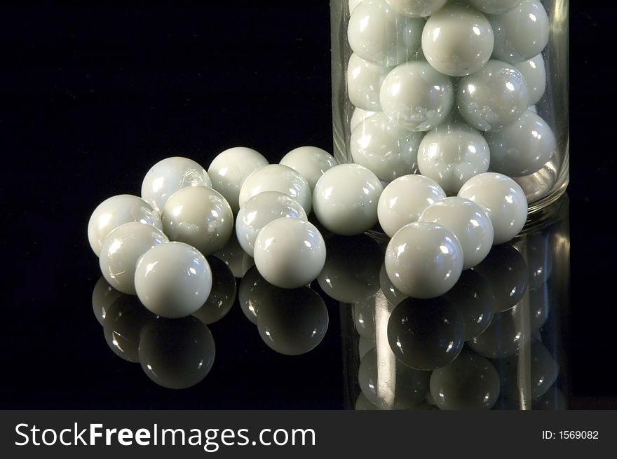 Some white pearls in a glass bottle reflecting on black. Some white pearls in a glass bottle reflecting on black