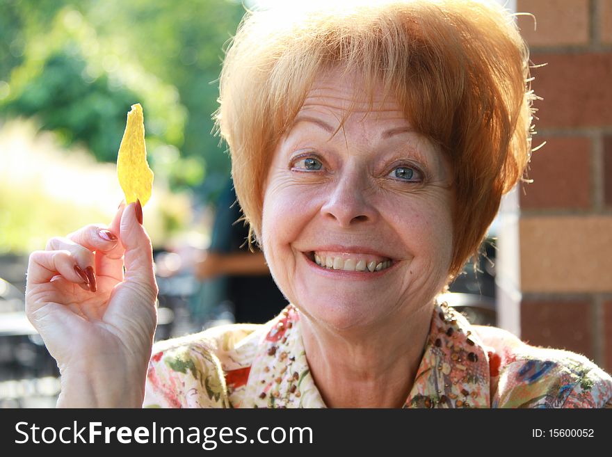A mature woman smiles at dinner while holding a tortilla chip. A mature woman smiles at dinner while holding a tortilla chip