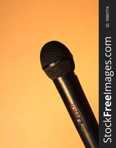 A modern black handheld ball head microphone on ginger background with copy space. A modern black handheld ball head microphone on ginger background with copy space