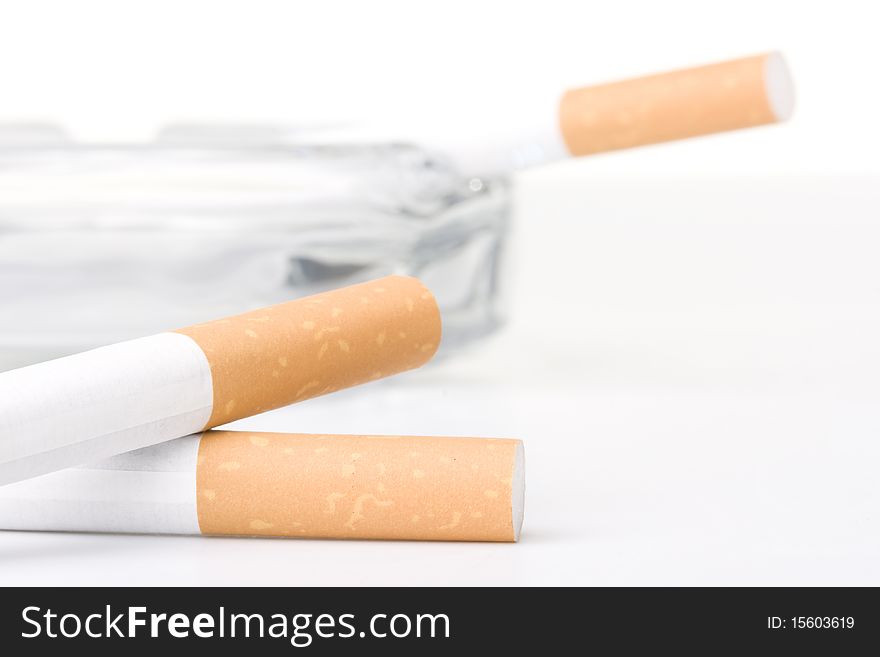 Two filtered cigarettes laying in front of an ashtray.