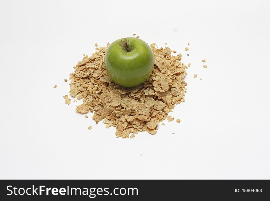 View from the top of fresh organic green apple placed on the top of heap of crunchy golden cereals isolated on white background. View from the top of fresh organic green apple placed on the top of heap of crunchy golden cereals isolated on white background