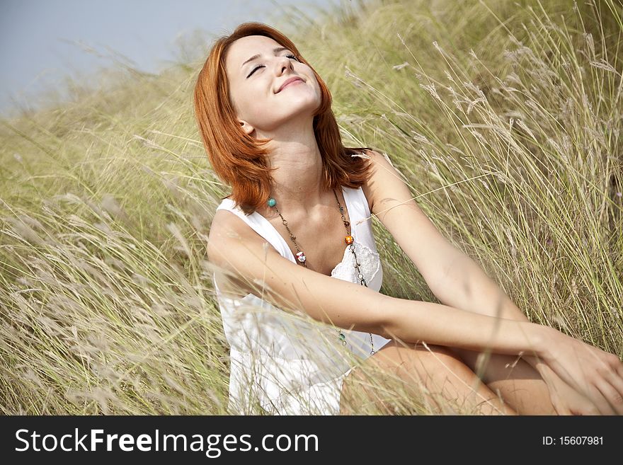 Beautiful red-haired girl at grass. Outdoor photo.