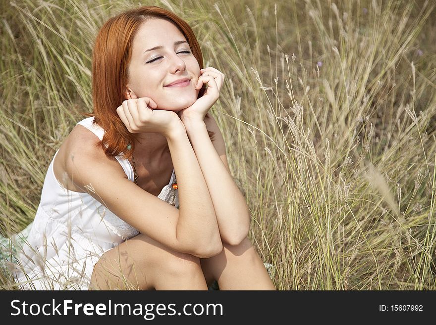 Beautiful red-haired girl at grass. Outdoor photo.