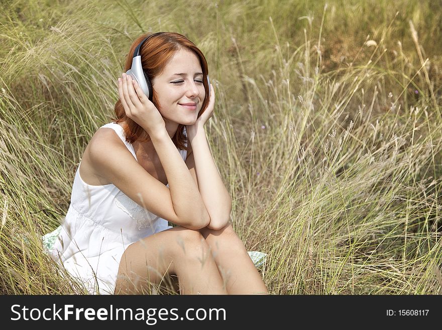 Beautiful red-haired girl at grass with headphones. Outdoor photo.