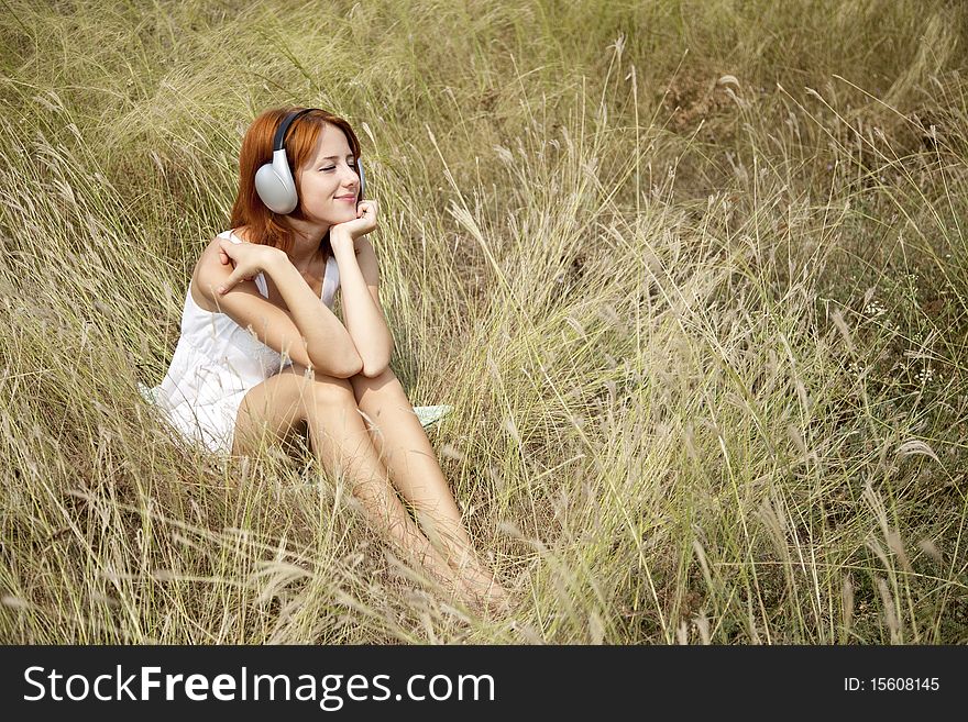 Beautiful red-haired girl at grass with headphones. Outdoor photo.