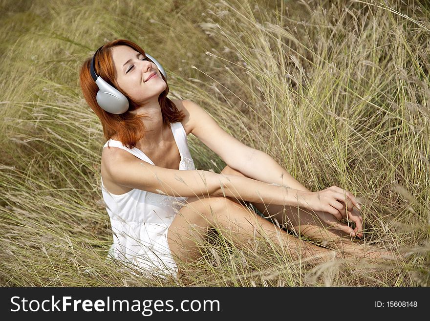 Beautiful red-haired girl at grass with headphones
