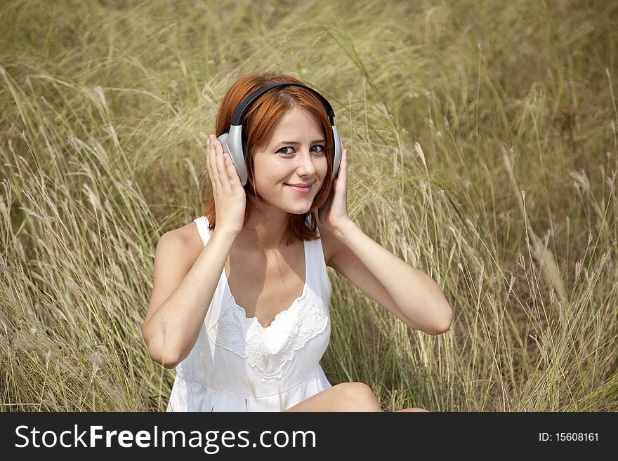 Beautiful red-haired girl at grass with headphones. Outdoor photo.