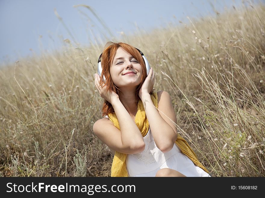 Beautiful red-haired girl at grass with headphones. Outdoor photo.