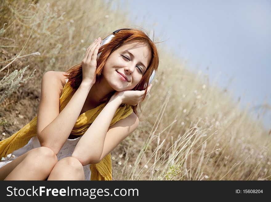 Beautiful red-haired girl at grass with headphones. Outdoor photo.