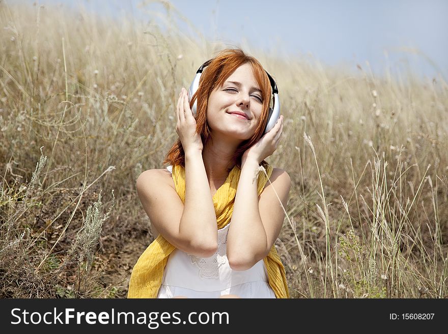 Beautiful red-haired girl at grass with headphones. Outdoor photo.