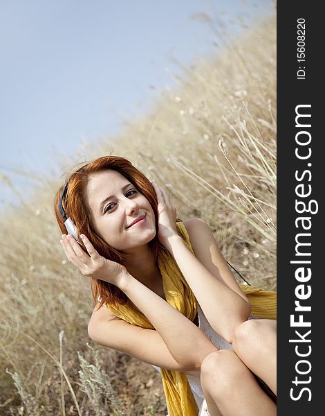 Beautiful red-haired girl at grass with headphones. Outdoor photo.