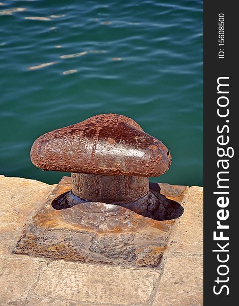 Rusty cleat detail, vertical photo, calm water in background