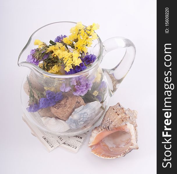 A glass jug full of dry flowers, wine corks ans sea shells with boardig tickets below it and big sea shell next to it on a light background. A glass jug full of dry flowers, wine corks ans sea shells with boardig tickets below it and big sea shell next to it on a light background
